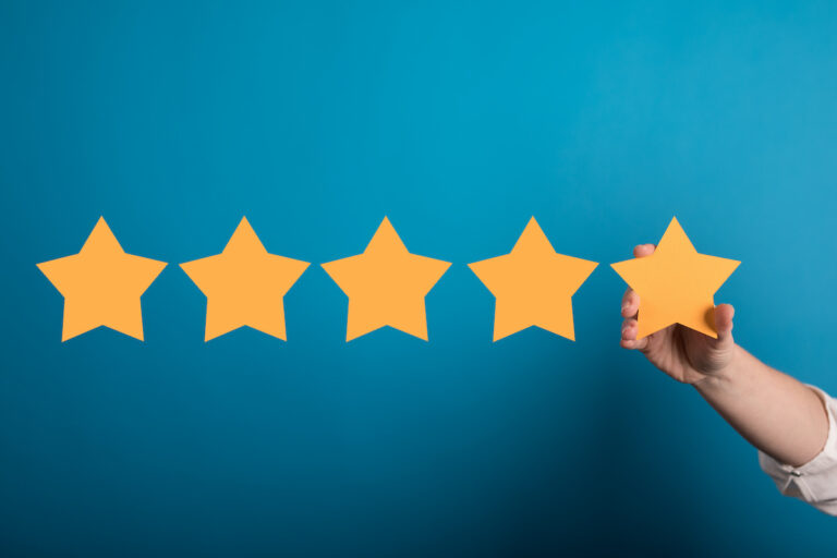 Bewertungsmanagement: Hand hält fünf Bewertungssterne vor blauem Hintergrund – Symbol für Vertrauen und positive Online-Reputation.
